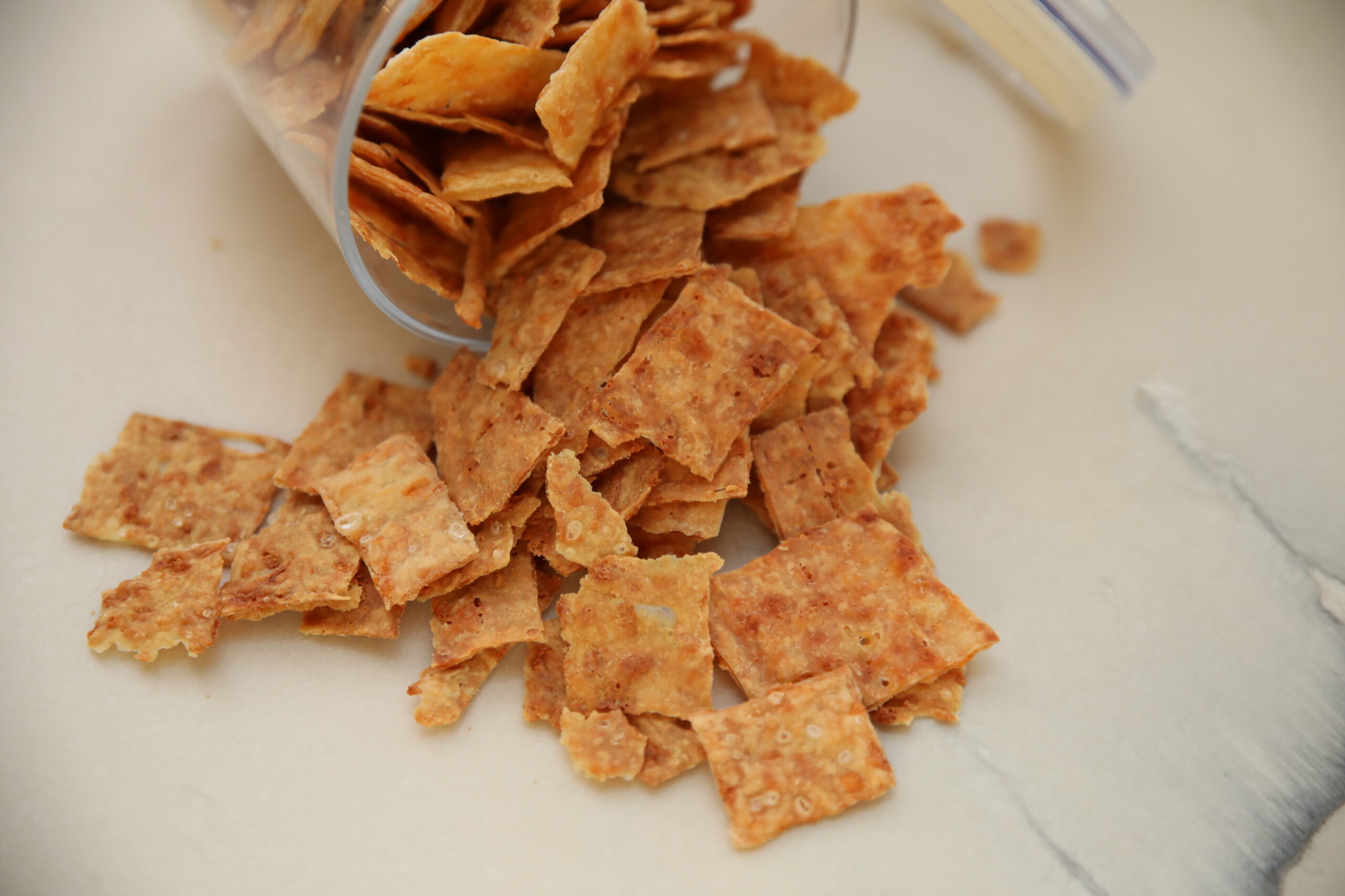 White marble countertop with sourdough discard crackers dumped out of a jar.